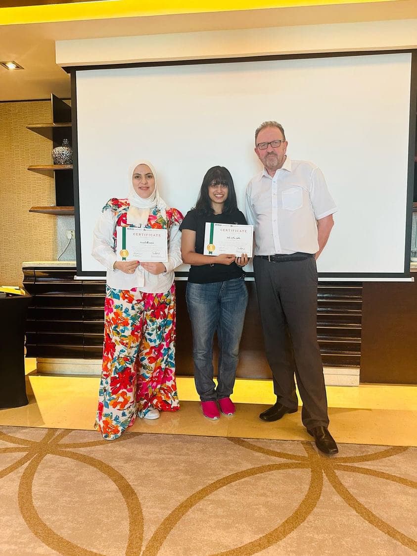 Two graduates proudly holding certificates presented by Dr. John Crimmins at a certificate ceremony